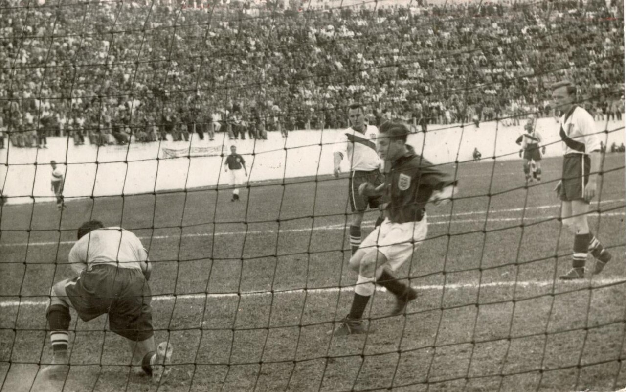Archival match photograph of England and the United States playing at the 1950 World Cup, seen through a goal net.